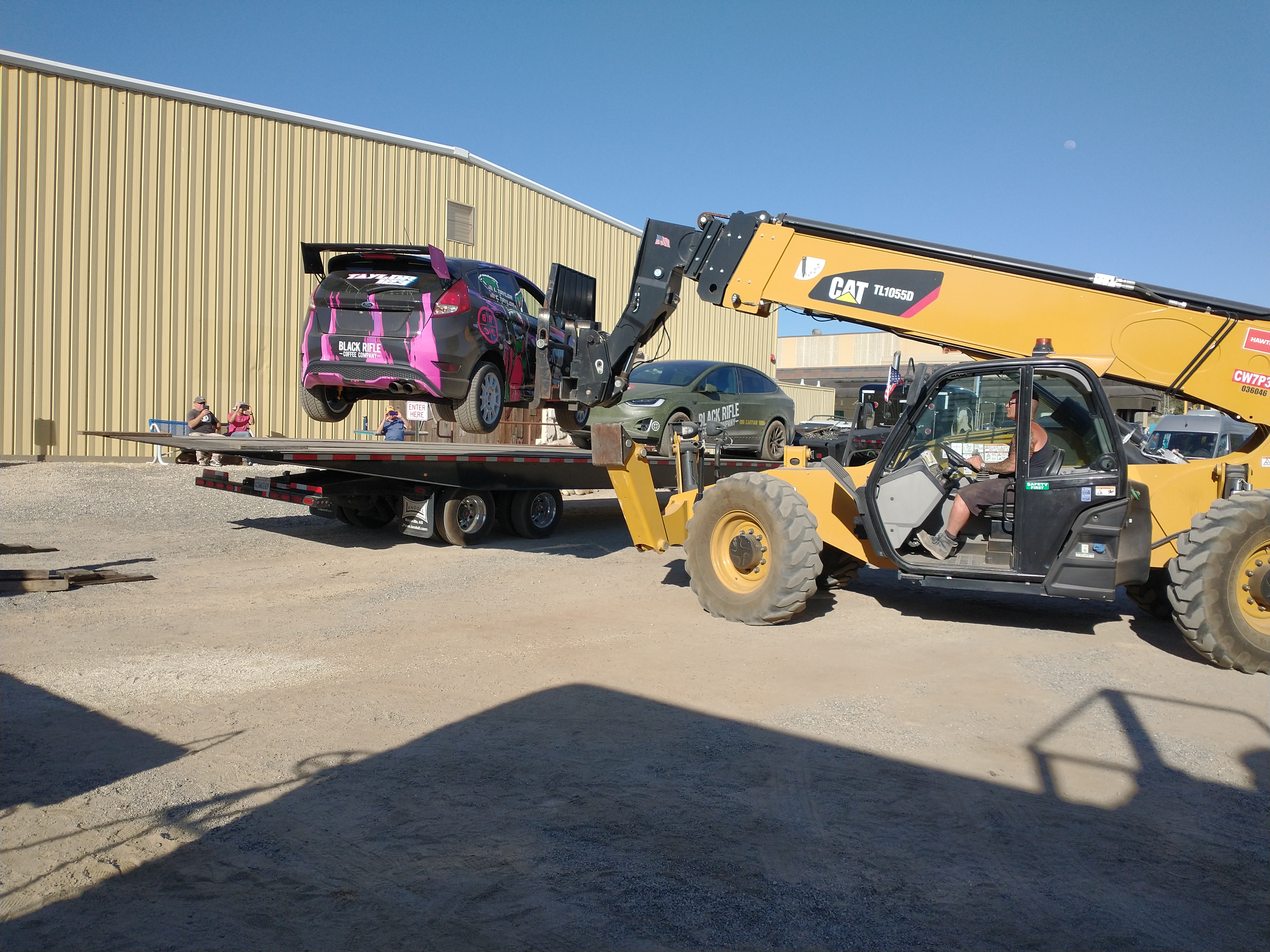 Forklift loading a Black Rifle Coffee decorated car onto a railroad flat car